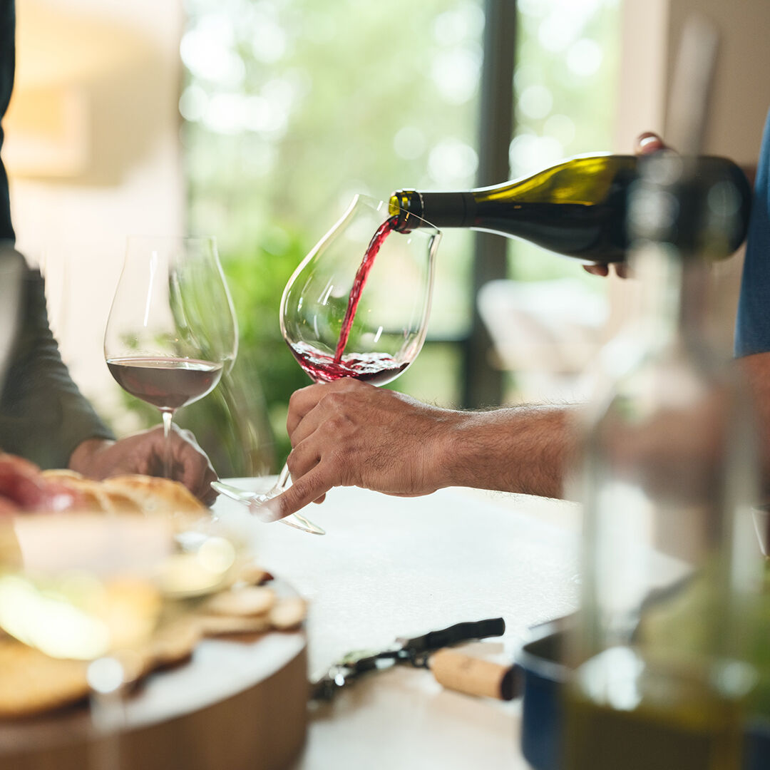 Gentleman pouring red wine in the kitchen.